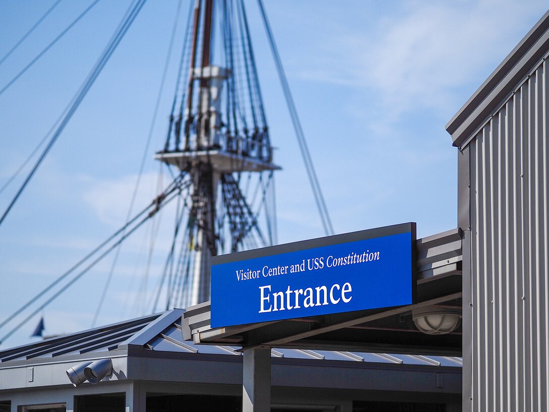 Sign welcoming visitors to the USS Constitution, with a ship's mast in the background.