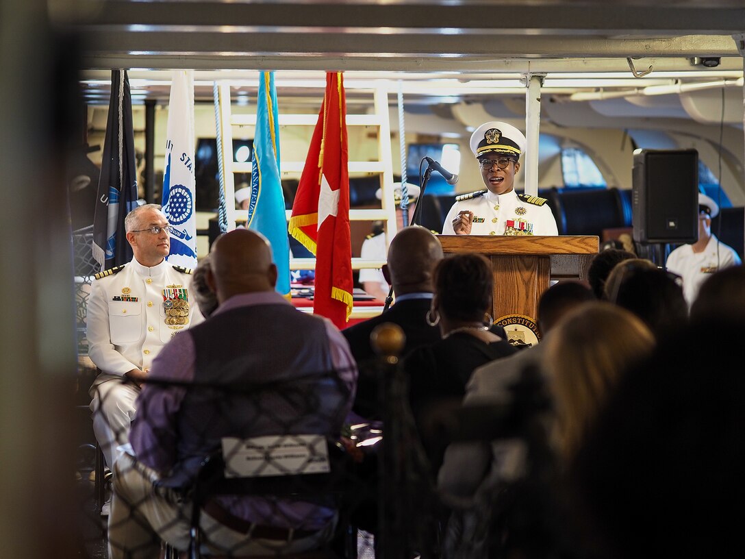 Navy office stands at a podium talking to a group.