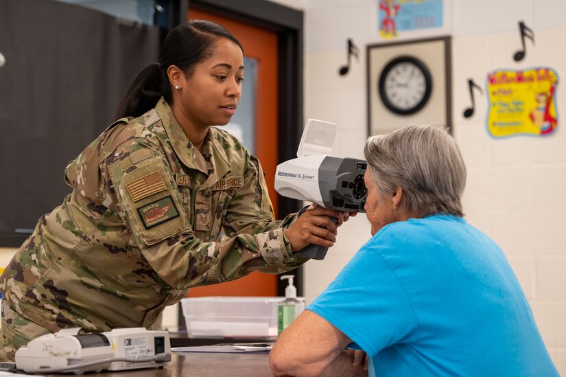 Staff Sgt. Praise Butler-Davis, 30th Medical Group optemetry technician, checks a patient's eyes during Innovative Readiness Training's Healthy Tennesseans event at Bledsoe County HIgh School in Pikeville, Tenn., June 4, 2023. The IRT program provides an array of services to communities in need including civil engineering, medical, and cybersecurity missions while also serving the service members who volunteer for the missions by providing real-world training opportunity to enhance readiness. Healthy Tennesseans is a medical mission providing no-cost services to local residents needing optometry, medical, dental, behavioral health and other care. (U.S. Air Force photo by Tech. Sgt. Kristen Pittman)