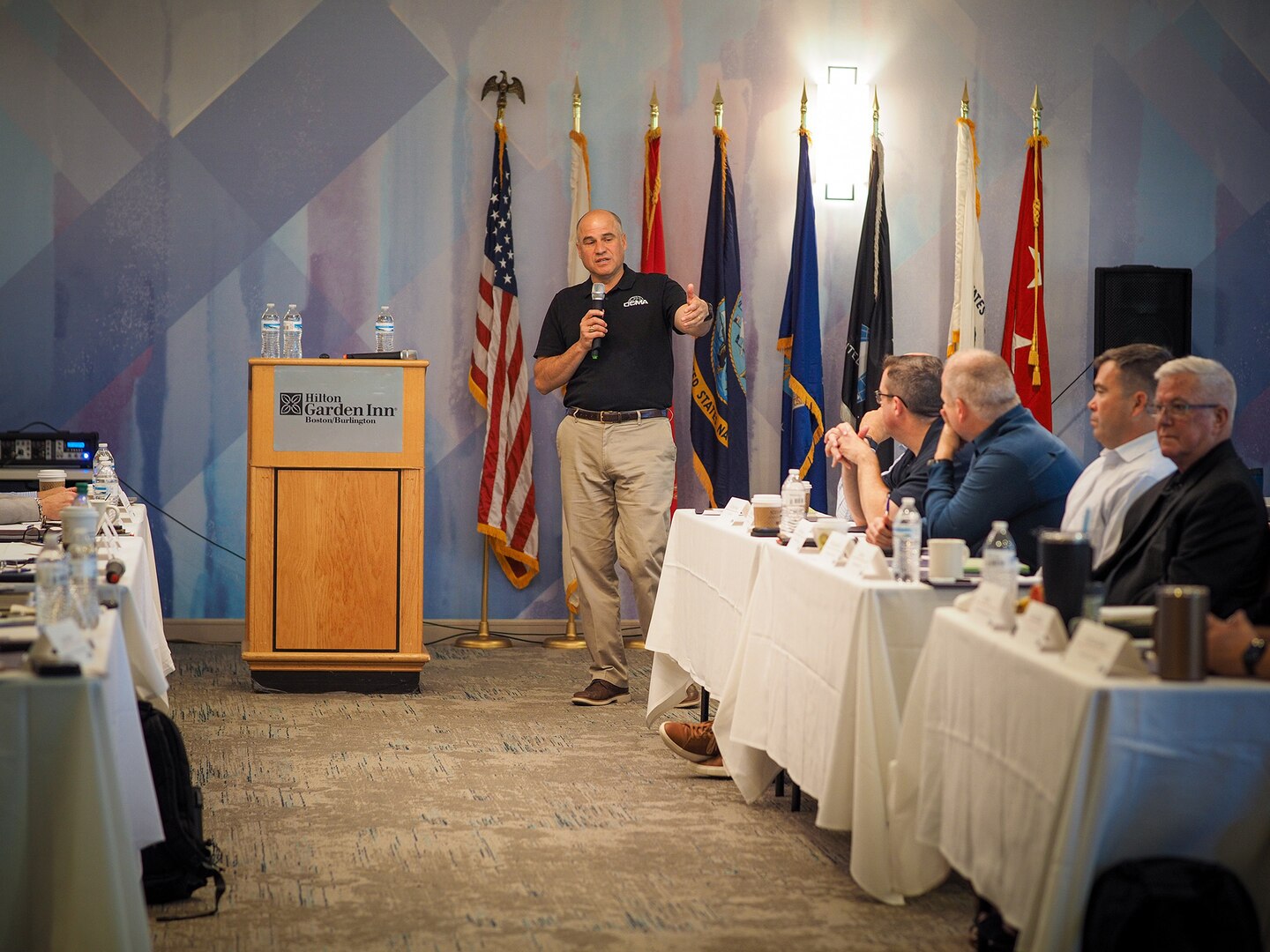 Man in blue shirt holds a microphone and talks to a room full of people