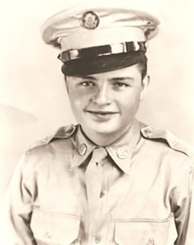 A soldier in a uniform and cap smiles for a photo.