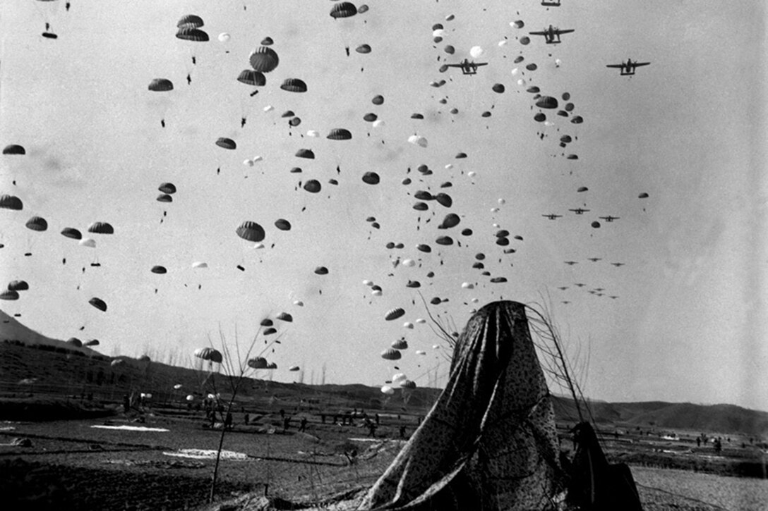 Parachutes billow from the sky as the airplanes they dropped out of fly past.