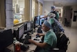 Three medical professionals sit at a desk reviewing images on computer screens