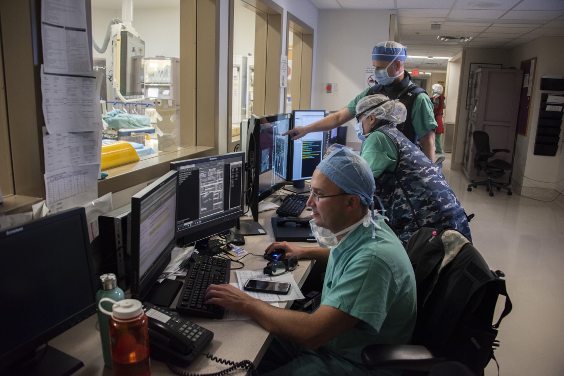 Three medical professionals sit at a desk reviewing images on computer screens