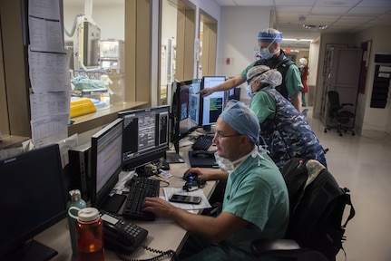 Three medical professionals sit at a desk reviewing images on computer screens