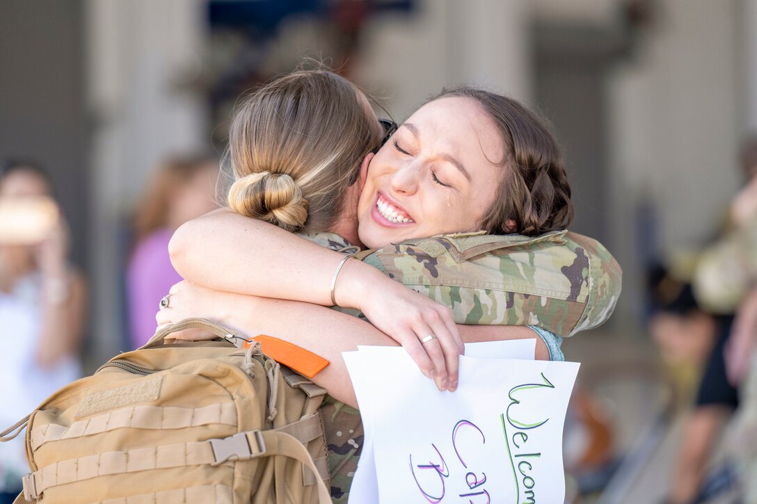A soldier hugs a crying loved one carrying welcome signs.