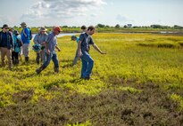 People walk across a field near water