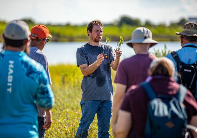People stand in a field with water while one person is holding two plants