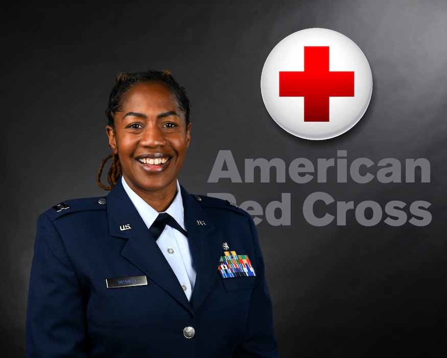 A formally dressed military nurse with a red cross logo behind her.
