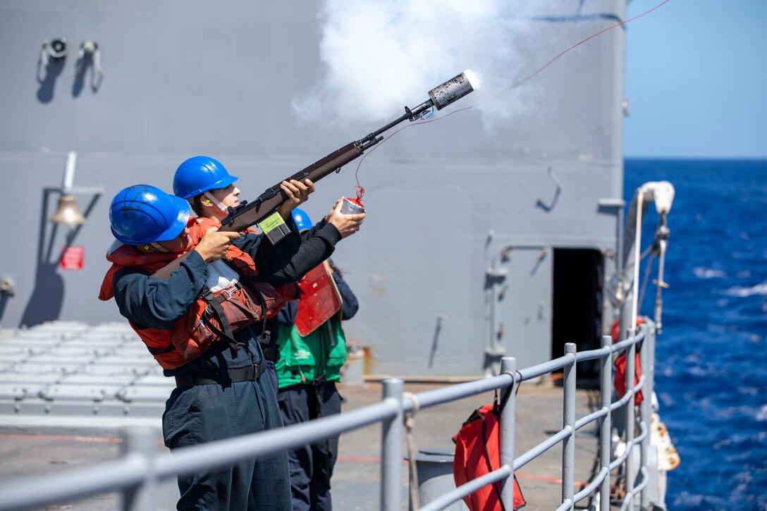 Sailors shoot a messenger line to another ship.