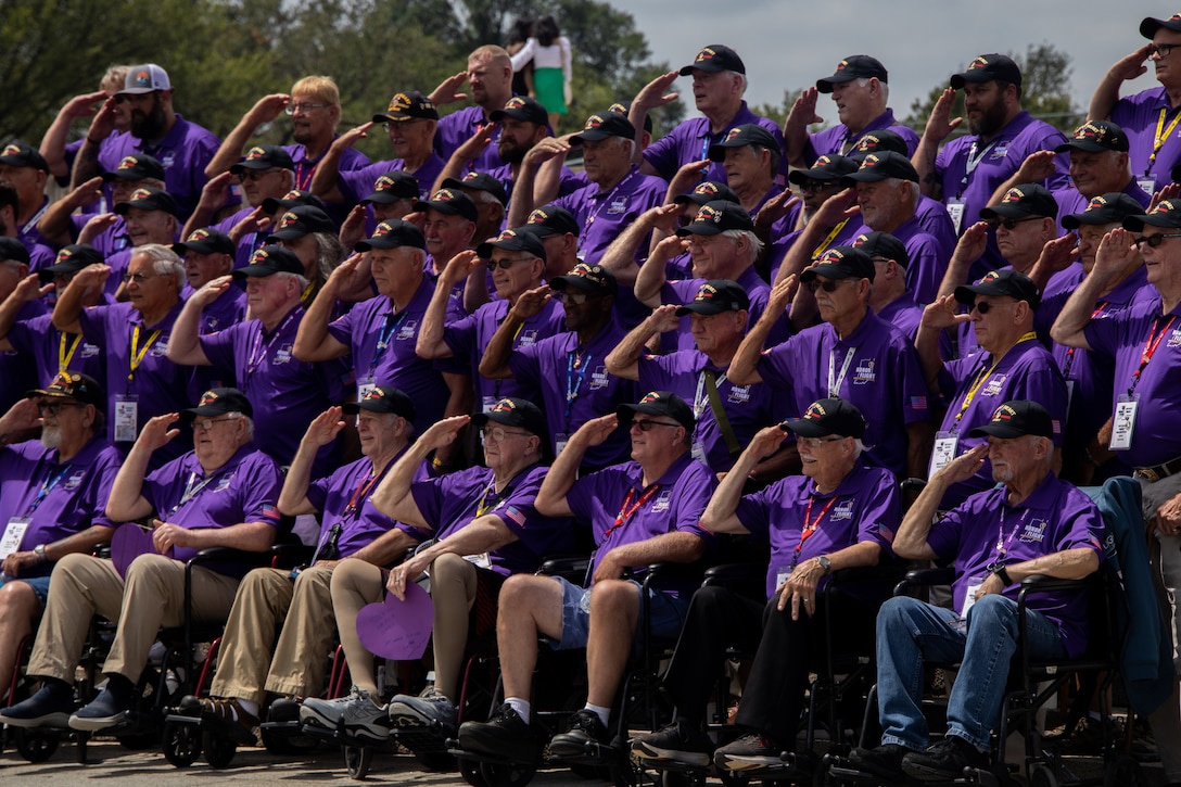 A large group of veterans in purple shirts salute as they pose for a picture.