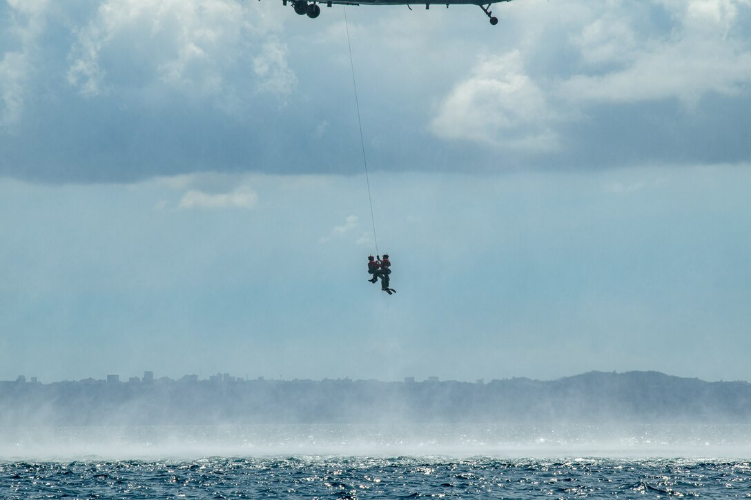 Two airmen are pulled from the ocean to a helicopter.