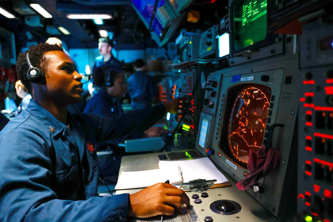 A sailor wearing a headset sits in front of monitors.