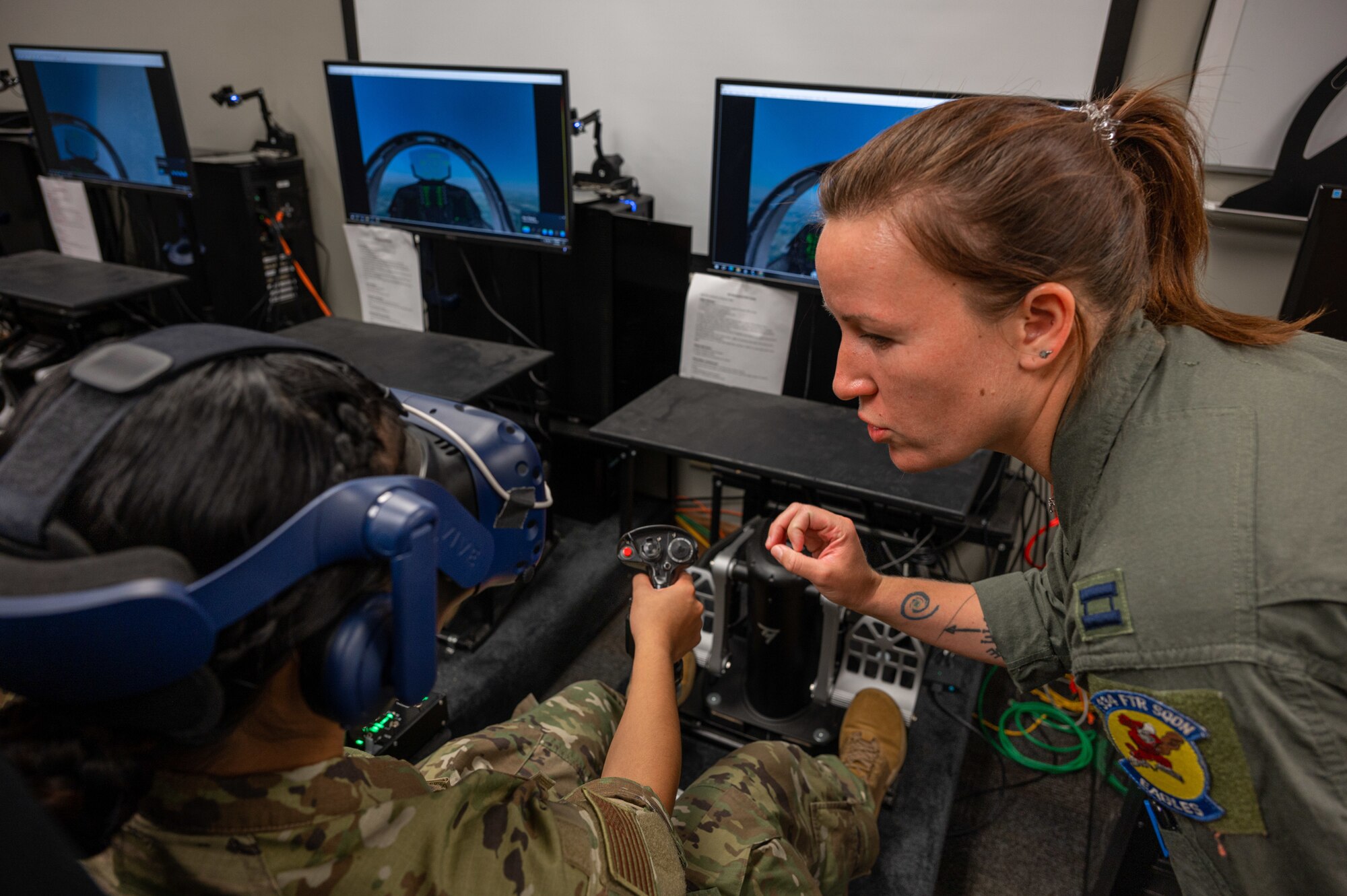 U.S Air Force Capt. Victoria Beck, 334th Fighter Squadron weapons safety officer, shows Air Force ROTC Academy Cadet Angelica Lumactod how to properly fly an F-15E Strike Eagle in a virtual reality training simulation at Seymour Johnson Air Force Base, North Carolina, August 3, 2023. Under the guidance of Capt. Victoria Beck, 334th Fighter Squadron weapons safety officer and Capt. Cecilia “Feisty” Tuma, a pilot assigned to the 333rd Fighter Squadron, the cadets attempted to take-off, attack both airborne and land targets and land during the simulation. (U.S. Air Force photo by Airman 1st Class Leighton Lucero)