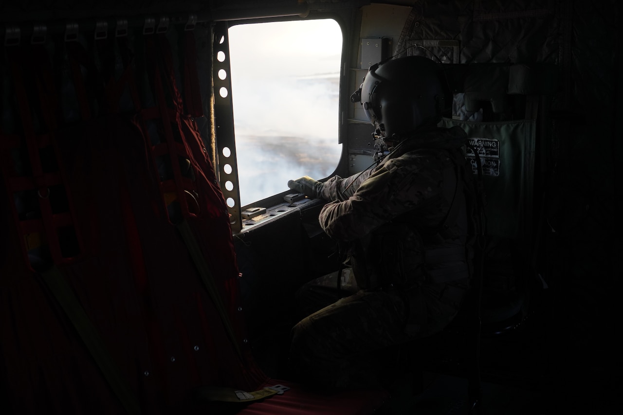 A service member looks out the window of a military aircraft.