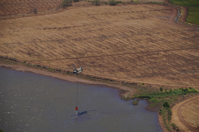 Two military aircraft perform aerial water bucket drops to battle wildfires in Hawaii.