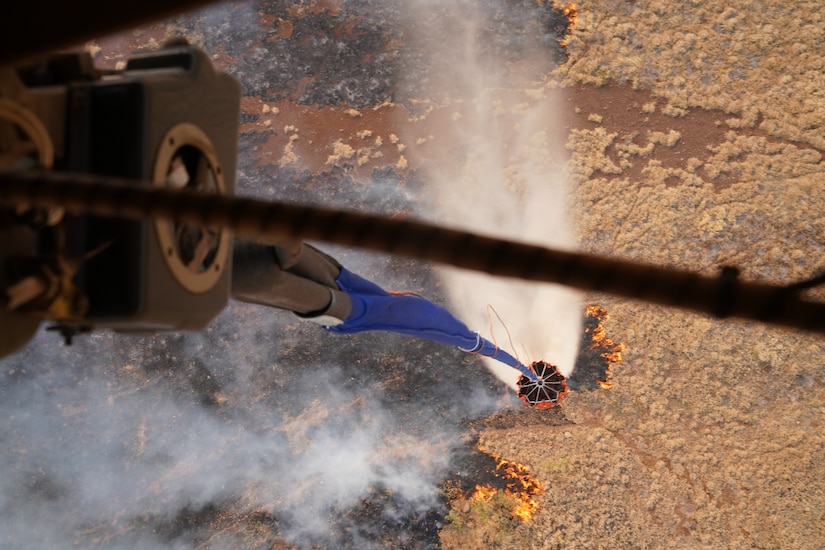 A military aircraft drops water over a wildfire.