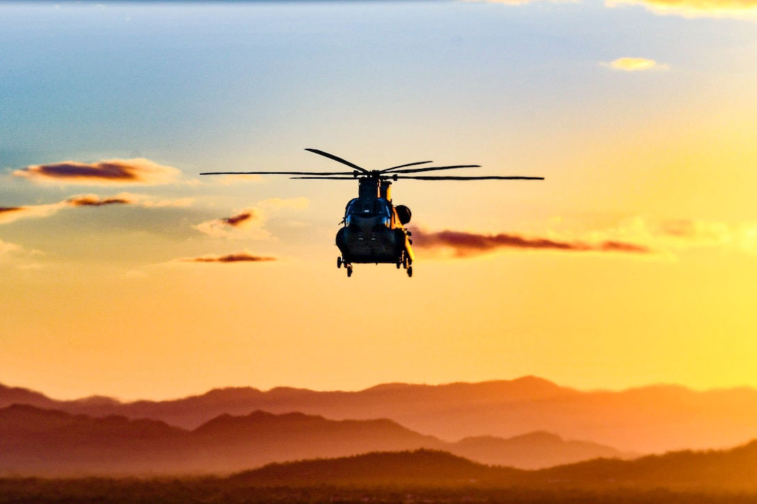 A helicopter flies through the sky above a mountain range.