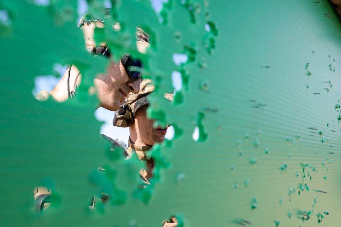 Two service members seen through bullet holes on a green target.