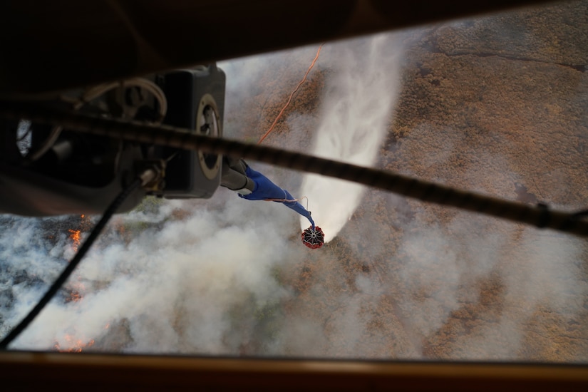 A military aircraft participates in an aerial water bucket drop to battle a wildfire.