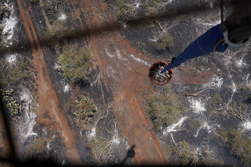 A military aircraft participates in an aerial water bucket drop to fight a wildfire.