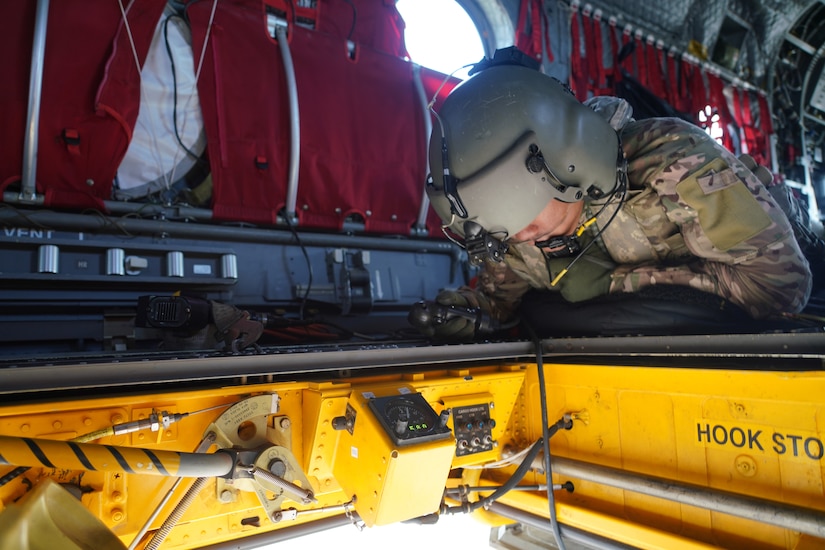 A service member looks through an opening on a military aircraft during an aerial water bucket drop over a wildfire.