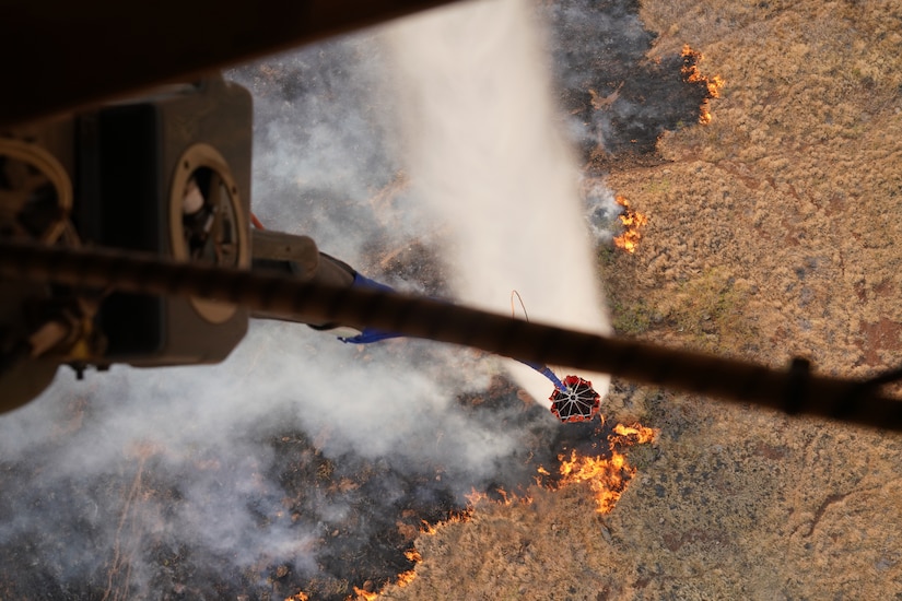 A military aircraft participates in an aerial water bucket drop to fight a wildfire.