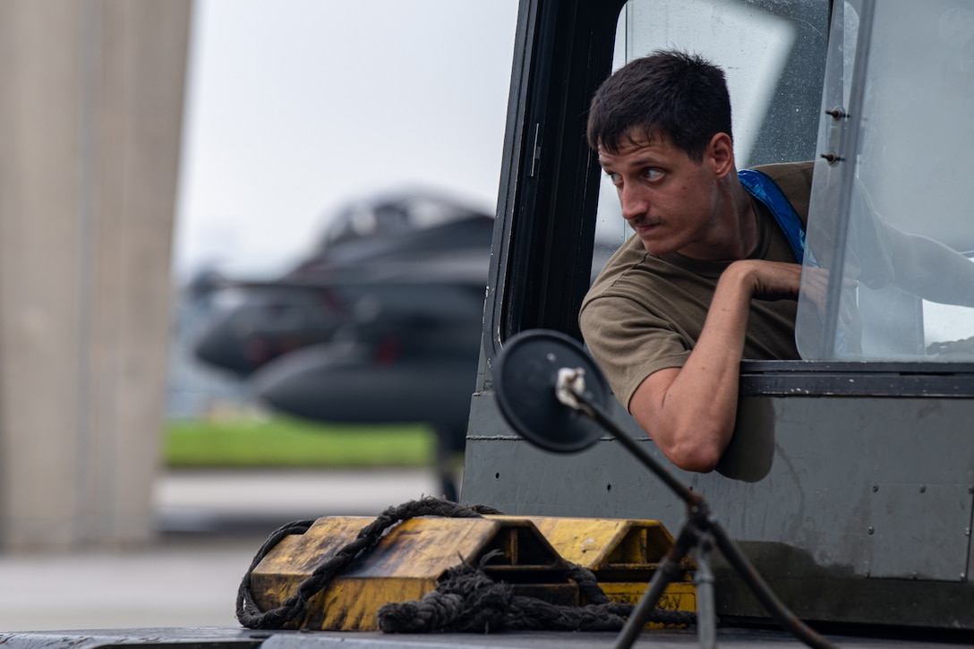 A service member leans out of the window of an aircraft towing vehicle.