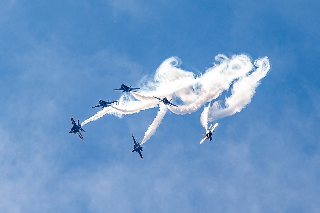 Six Navy aircraft perform aerial maneuvers, forming trails in the sky.