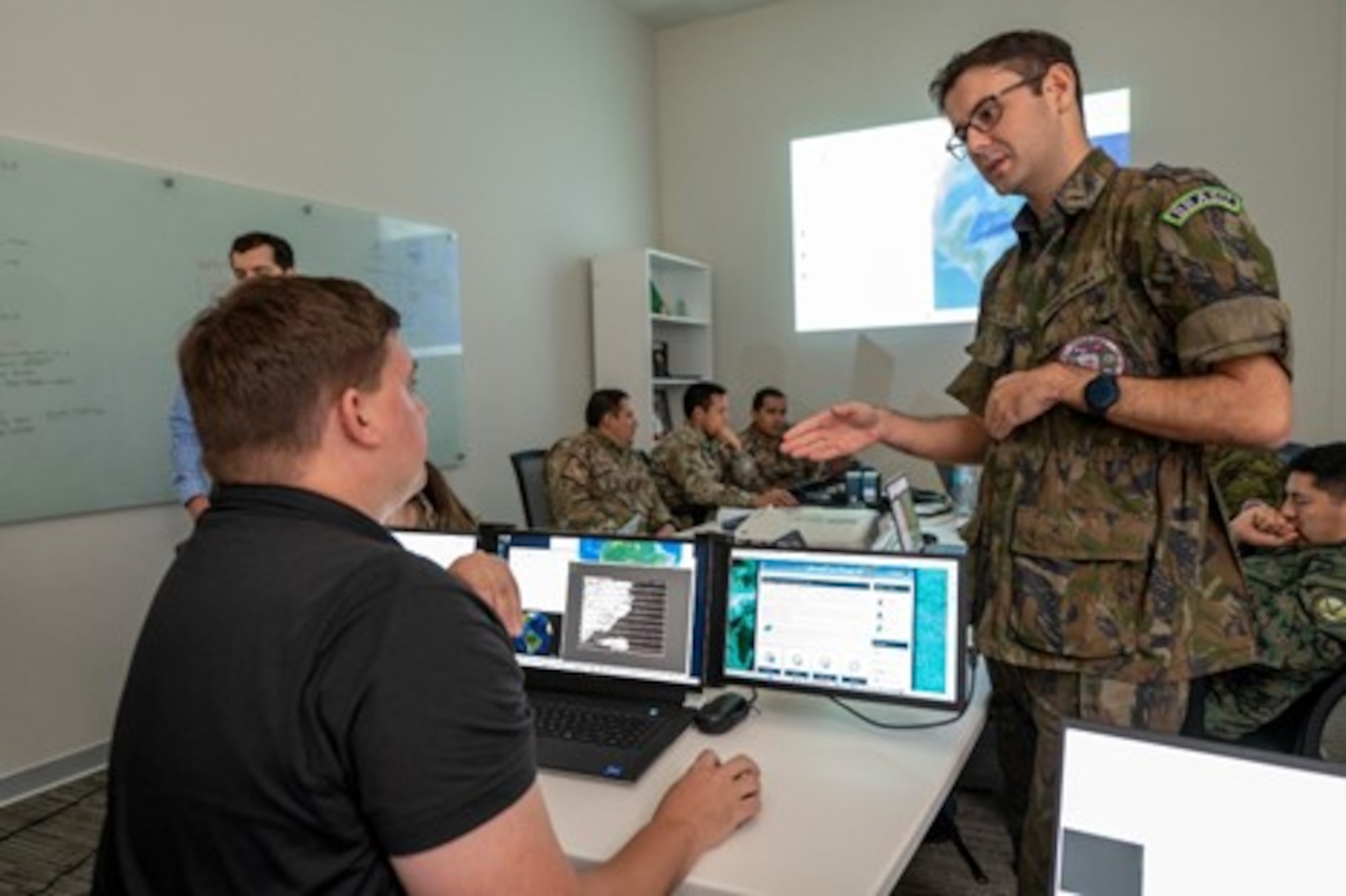 Space Systems Command Surveillance, Reconnaissance and Tracking (SRT) team member Adam Woodard shows Lt. Fabio Rocha Brazil, how to determine the best sensor type to use while the SRT team builds Operational Planning Products. Photo credit: SSgt Matthew Matlock