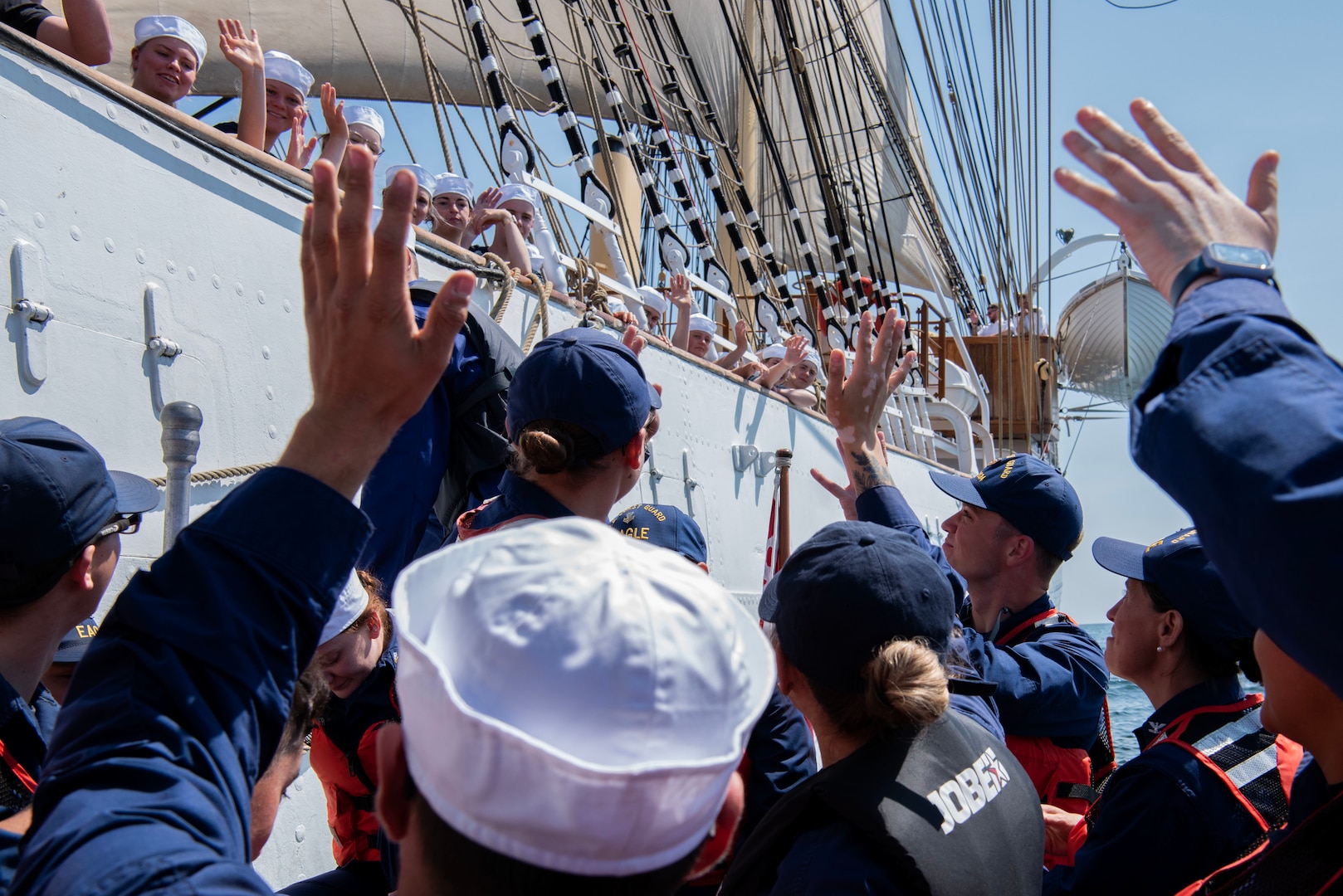USCGC Eagle (WIX 327) crewmembers wave from a small boat to the trainees aboard the Danish training ship Danmark after taking tours aboard the ship, June 14, 2023, in the Baltic Sea. Eagle is a tall ship used as a training platform for future Coast Guard Academy officers as well as a vessel utilized for establishing and maintaining domestic and international relationships. (U.S. Coast Guard photo by Petty Officer 3rd Class Carmen Caver)