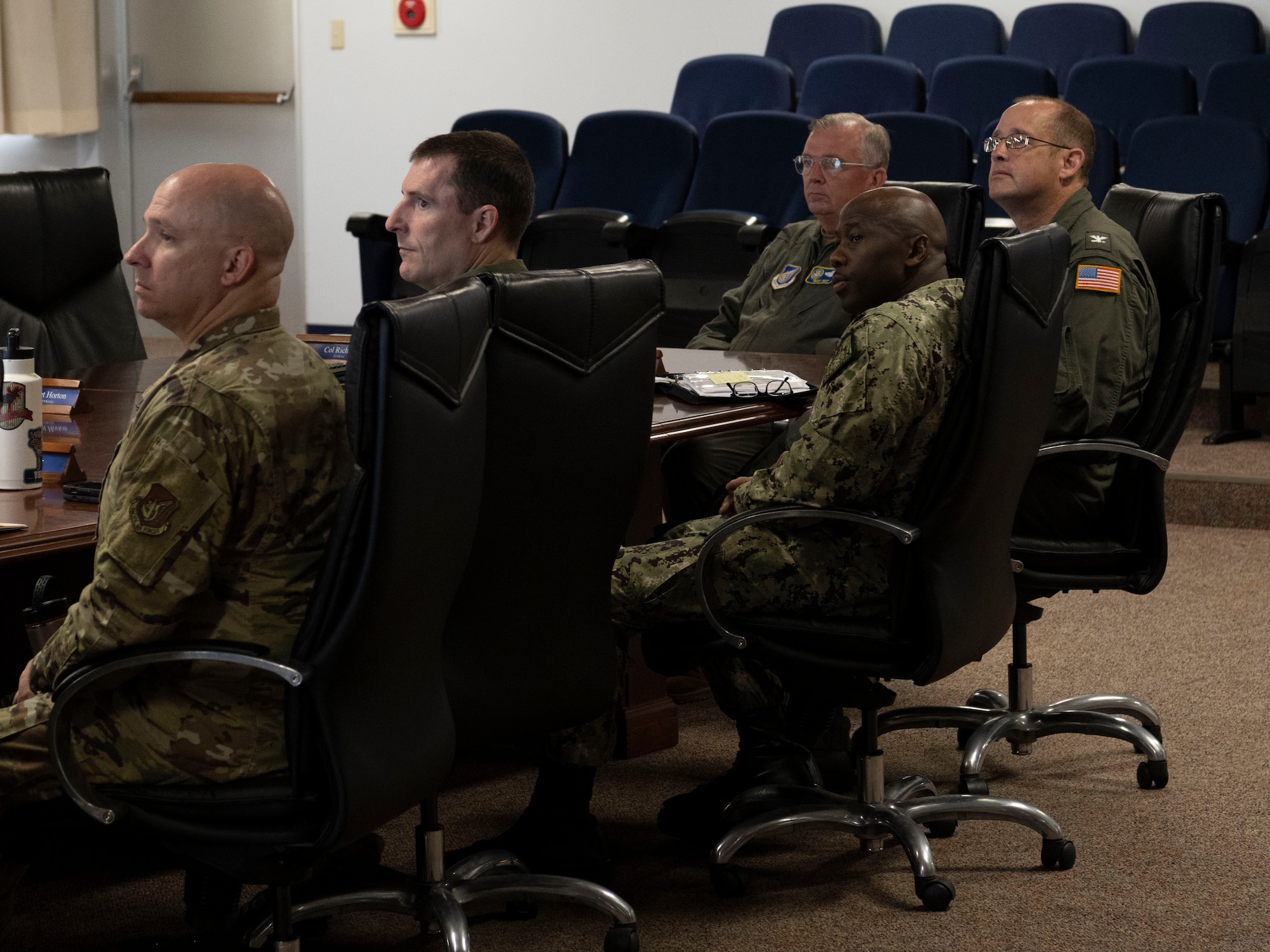 Military members sitting at a table as a brief is given.