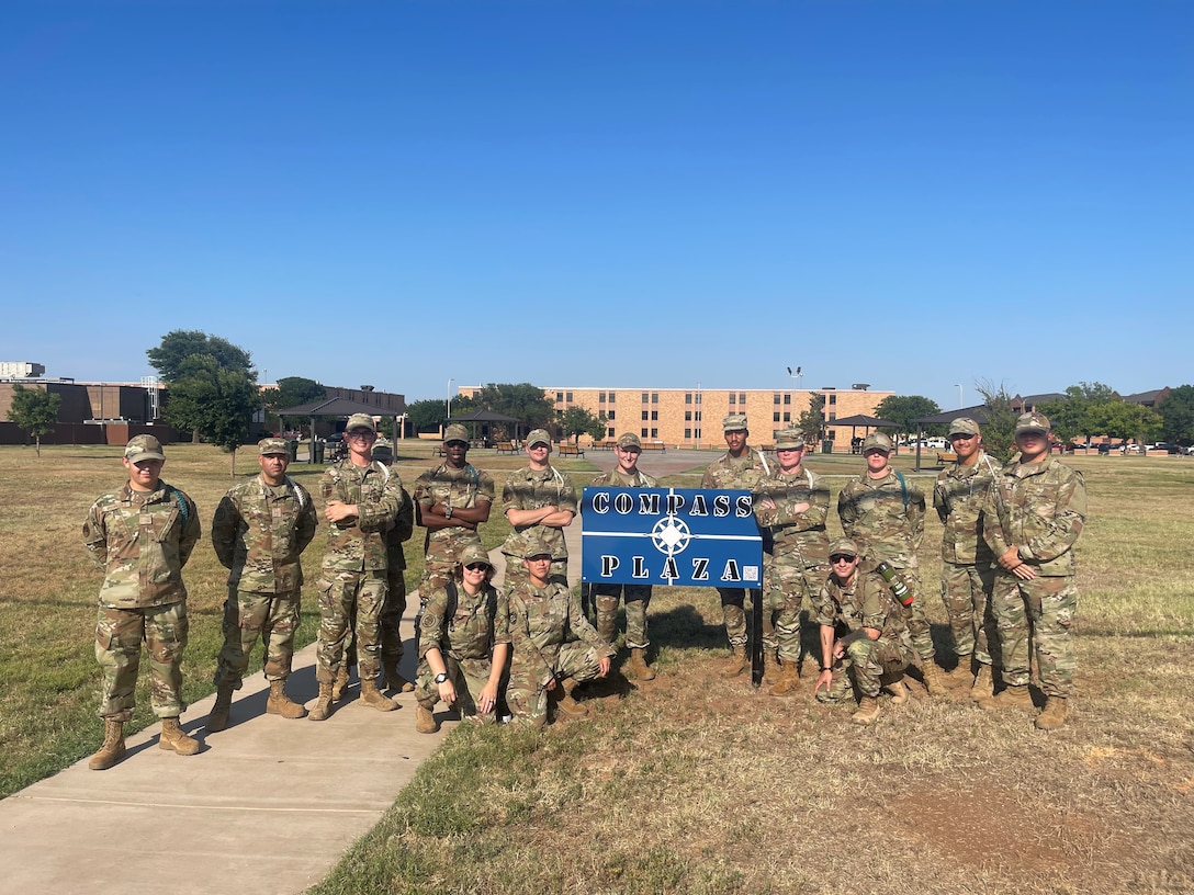U.S. Air Force Airmen in Training gather around a blue sign that reads "Compass Plaza.