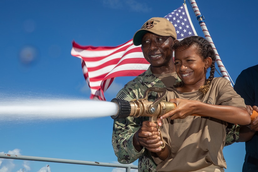 A sailor and child operate a firefighting hose aboard a Navy ship during family day.