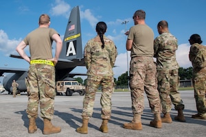 five people look at a vehicle being loaded into a C-130H