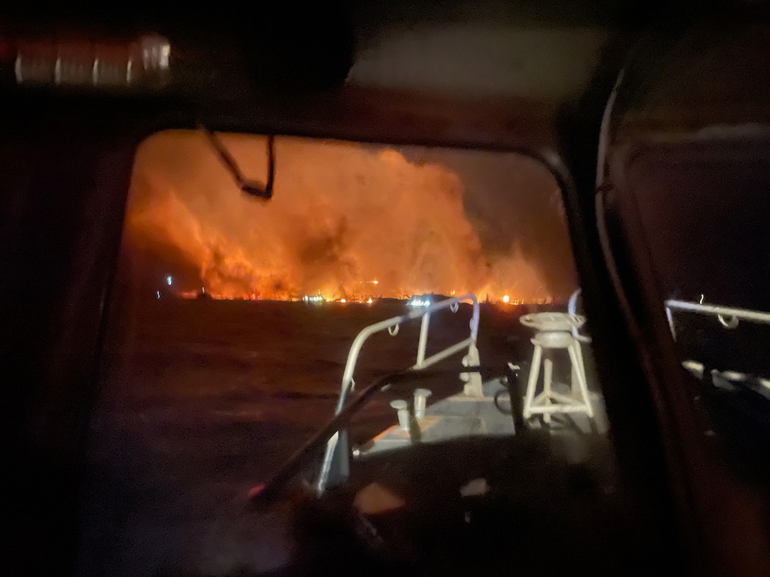 The view from a Coast Guard vessel sailing at night as a wildfire burns in the distance.