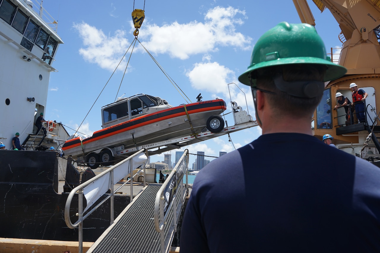 A crew member watches as a small boat is loaded onto a Coast Guard vessel.