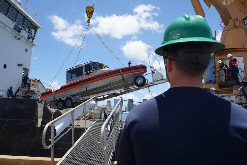 A crew member watches as a small boat is loaded onto a Coast Guard vessel.