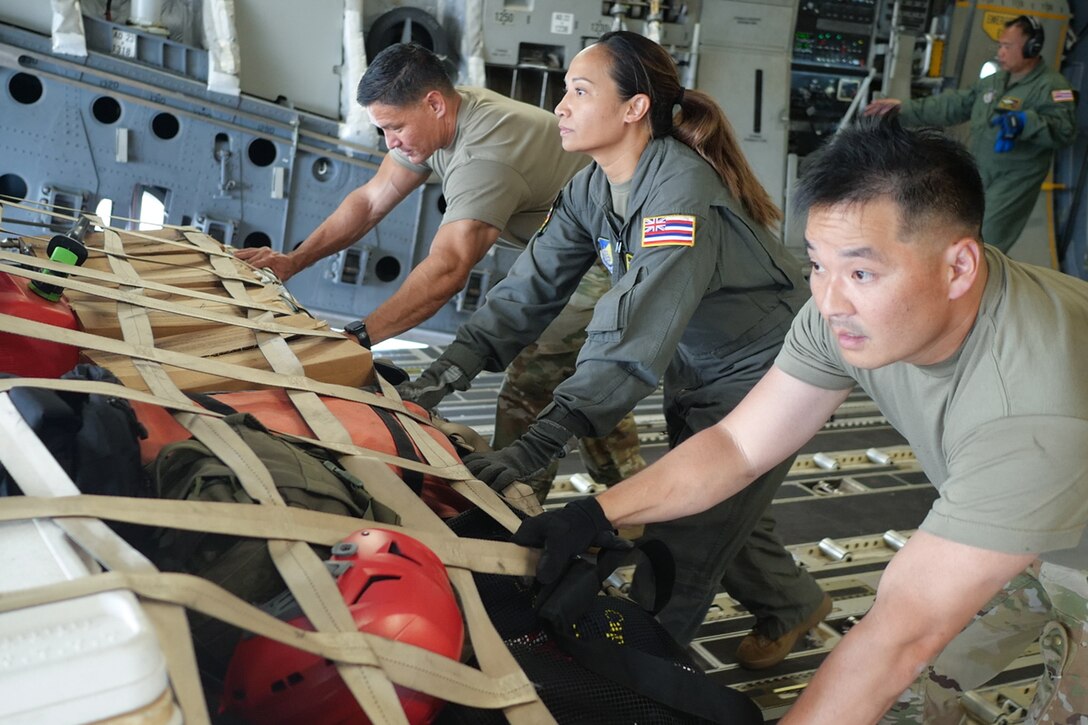Airmen push cargo from inside a military aircraft.