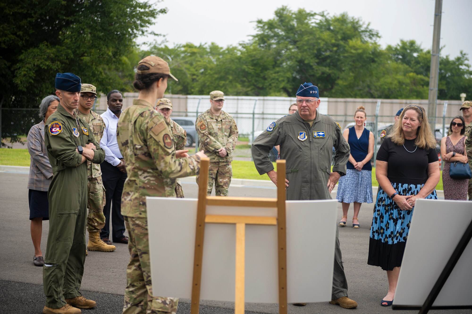 Military members standing in front of poster boards during a briefing.
