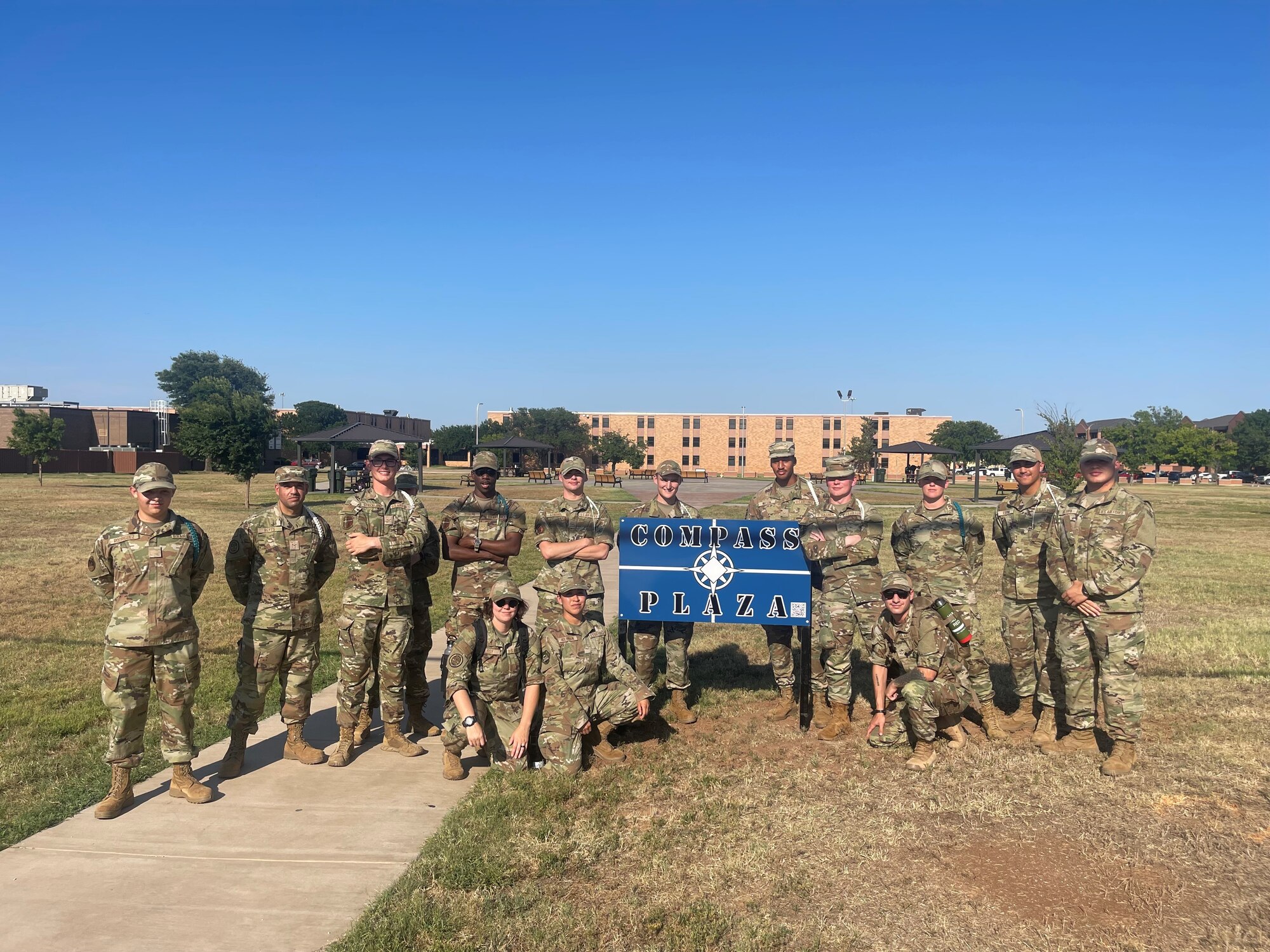 U.S. Air Force Airmen in Training gather around a blue sign that reads "Compass Plaza.
