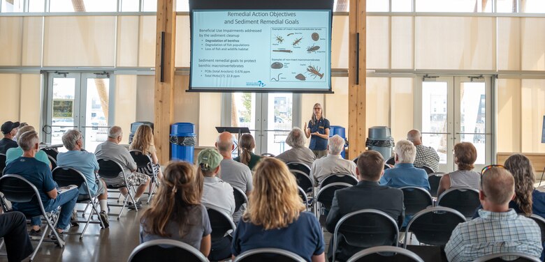 A woman gives a presentation in front of a crowd in a pavilion.