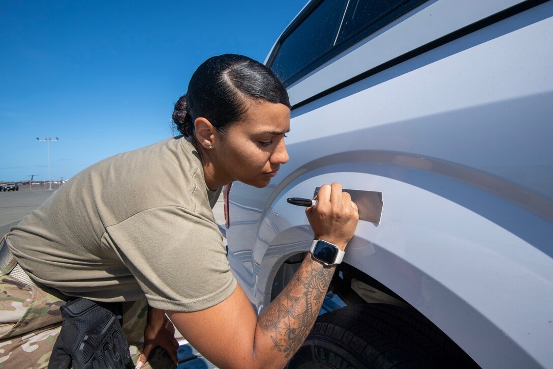 An airman writes on a piece of tape attached to a car.