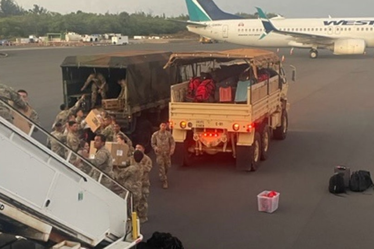 Service members offload supplies from a military aircraft onto military vehicles.