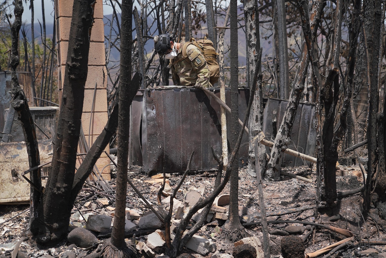 A service member looks through rubble left behind by a wildfire in Hawaii.
