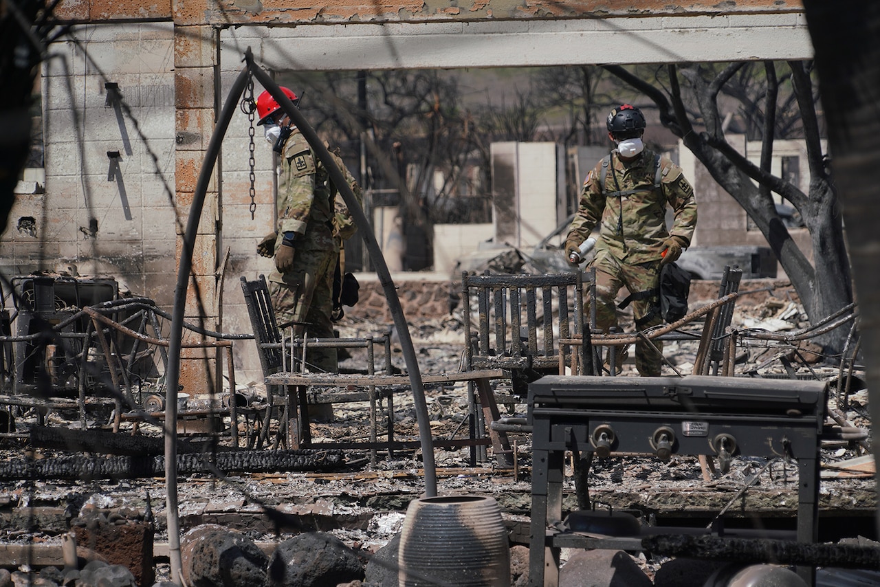 National Guard members assess wildfire damage in Maui, Hawaii. Burnt furniture can be seen in the rubble.