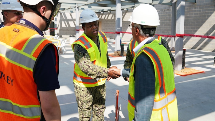 A naval officer shakes hands with a company CEO on a construction site.