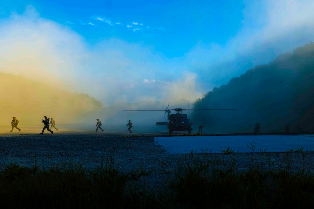 Service members exit a parked helicopter and run on either side of the aircraft.