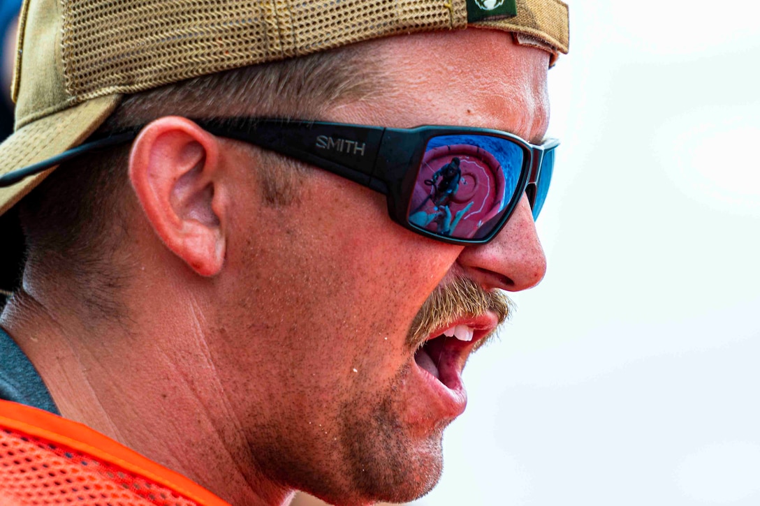 An airman wearing sunglasses speaks; a person on a raft can be seen in the reflection of his sunglasses.