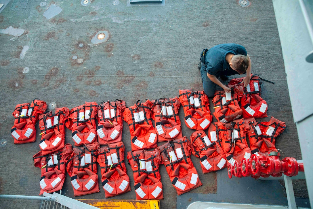 A sailor works on flotation vests lined up in two rows.